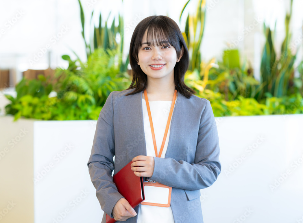 グレーのジャケットを着て赤いノートを持つ女性